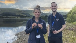 2x Rangers, Helen Rountree on left and Josh Mackin on right, pictured at Gladhouse in front of the reservoir holding binoculours
