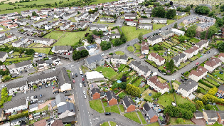 Drone image of residential area showing houses, roads, and green spaces.